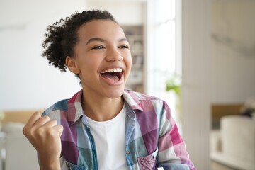 Excited mixed race teen girl makes yes winner hand gesture, celebrates success, personal achievement