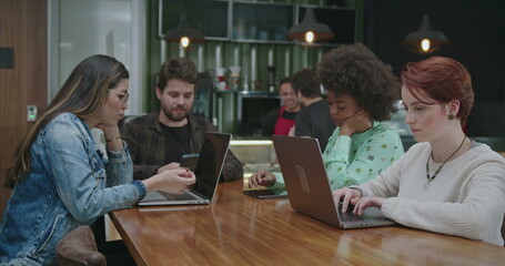 Group of people seated at coffee shop in front of laptop computers. Young millennials working or studying remotely using modern technology devices