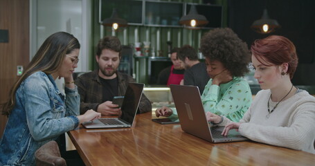Fototapeta premium Group of people seated at coffee shop in front of laptop computers. Young millennials working or studying remotely using modern technology devices