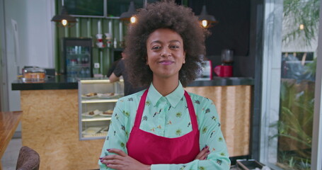 One black woman employee with arms crossed standing at coffee shop smiling at camera