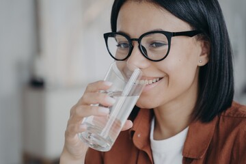 Happy thirsty young woman in glasses holding glass, drinking filtered clean water. Healthy lifestyle