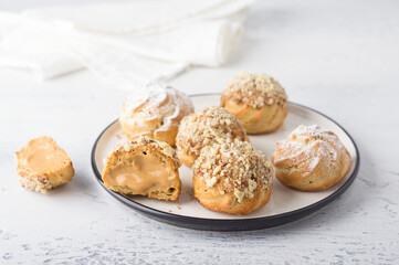 Gluten-free oat profiteroles with caramel cream of boiled condensed milk, sprinkled with powdered sugar and nuts on a light blue background. Delicious homemade food