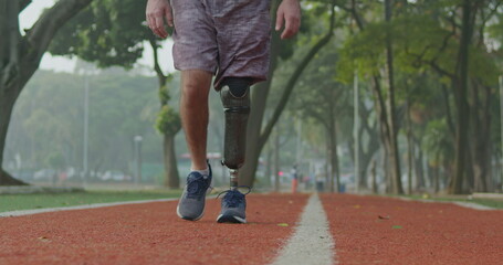 Front view of a middle aged disabled athlete man with prosthetic leg walking forward toward camera outdoors on running track