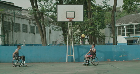 Two paraplegic disabled athletes playing basketball outdoors passing ball to team member. Determination and sport with disability concept