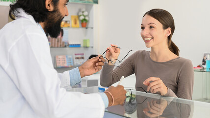 Obraz premium Happy young woman choosing eyeglasses frame in optical store. Eyesight and vision concept