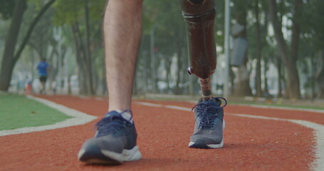 Front view of a disabled athlete walks outdoors with prosthetic leg. Male person with disability