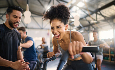 Gym, fitness and woman on bike with personal trainer for motivation, support and power workout, cheering and clapping hands. Coach, black woman and cycling exercise at sport center, sweat and energy