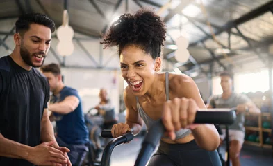 Foto auf Acrylglas Gym, fitness and woman on bike with personal trainer for motivation, support and power workout, cheering and clapping hands. Coach, black woman and cycling exercise at sport center, sweat and energy © N F/peopleimages.com