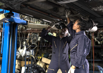 Black mechanic man and african mechenic woman working and fixing underneath car in auto repair, Car Mechanic Concept