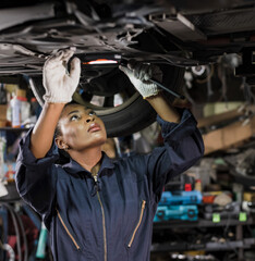 Black mechanic woman working underneath car fixing in auto repair shop, Car Mechanic Concept