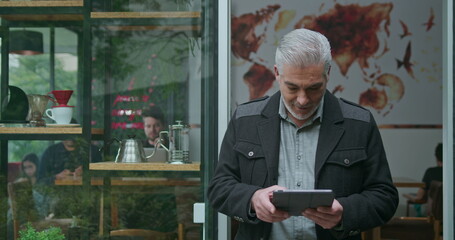 A middle aged entrepreneur owner of coffee shop managing business looking at tablet device. Portrait of an older manager using modern technology