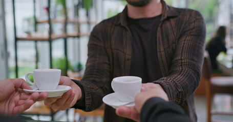 Happy male customer getting up from table and picking up two orders of espressos at coffee shop counter. Male colleague handing cafe to female colleague