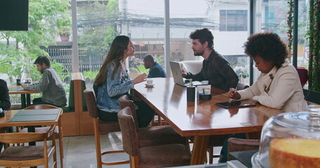 Group of people inside coffee shop. Female friend handing espresso to male colleague sitting at cafe restaurant table. Men and women customers together at cafe place