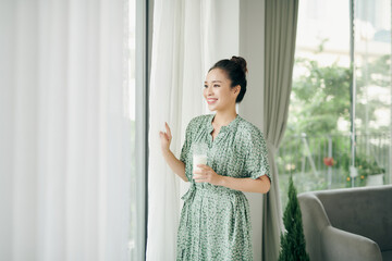 Asian lady drinking glass of milk while looking out the window with copy space