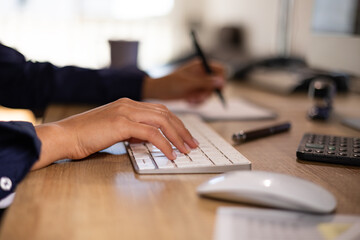 Woman types on the keyboard and writes notes on a page. Desk with calculator and office implements. Calculating, accounting, clerk, financial business and back office.