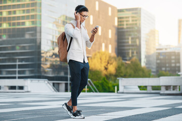 Fototapeta na wymiar Phone, music and city with a man student walking to university or college during his morning commute. Headphones, social media and 5g mobile technology with a male pupil in an urban town for a walk