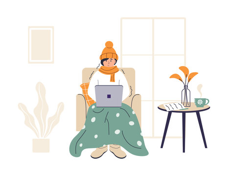 Young woman wrapped in plaid is working on laptop. Low temperature at home. Person freezes from cold warming up with hot drink. Girl sitting in chair in warm clothes. Frozen and shivering character.