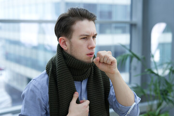 Sick ill guy, young man coughing in his fist, hand, suffering from cough, bronchitis indoors....