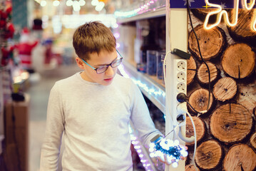 Christmas decoration shopping. Caucasian boy in eyeglasses choose Christmas lights in shopping mall