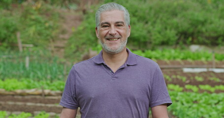 One happy senior man standing in green field background. A middle aged 50s male closeup face outdoors in small farm