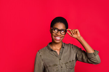 Portrait of attractive cheerful minded girl touching specs deciding copy space isolated over vivid red color background