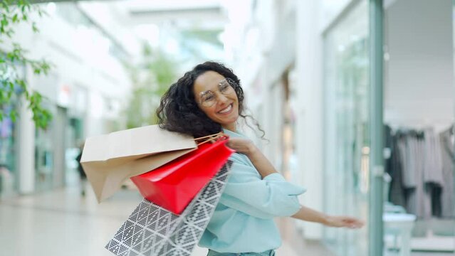 Portrait of cheerful young shopaholic woman holding paper bags with purchases and smiling at camera standing on shopping center. Happy lady shopping on black friday joyfully jumps for joy enjoys