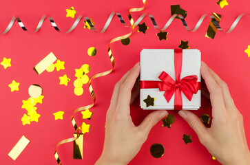 White gift box in female hands on a red festive background, copy space