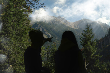 The guy shows the way to the girl in the forest in the mountains. Guy pointing to the horizon in the mountain. Mountaineer pointing to the path. Silhouette of two people on a background of mountains.