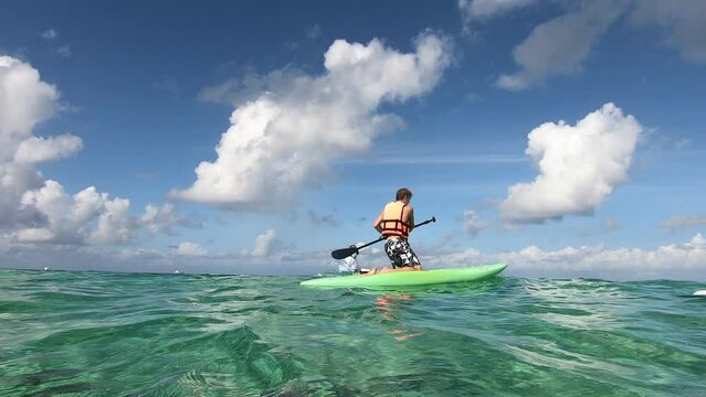 Boy enjoying Paddle-board near a beach under watch of life guard | Boy with life jacket using Paddle-board surfing near a beach under watch of life guard