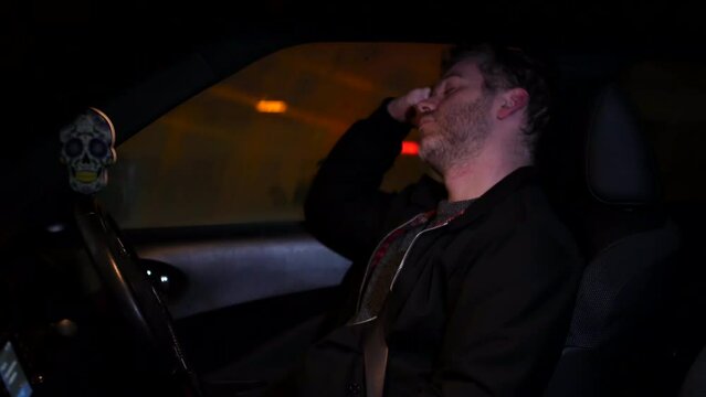 A man sleeping in his car at n ight next to a busy road in a city