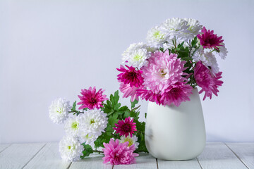 A bouquet of beautiful chrysanthemum flowers in a white vase on a white wooden table
