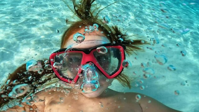 Underwater selfie of young red hair girl with diving mask holding camera while having fun in crystalline turquoise sea water. Slow motion
