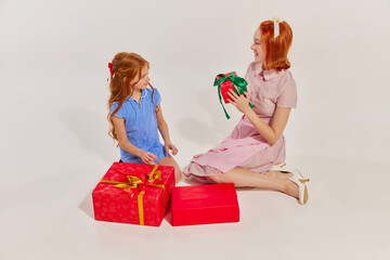 Portrait of beautiful woman, mother giving present to her daughter isolated over grey studio background. Winter holidays
