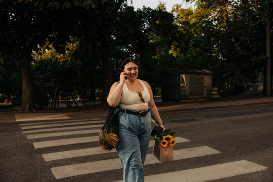 Smiling woman talking on mobile phone while walking on zebra crossing