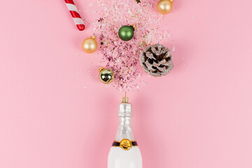 A Christmas tree ball in the shape of a white champagne bottle. Glitter, green and golden Christmas tree baubles, candy canes and pine branches come out of this bottle.