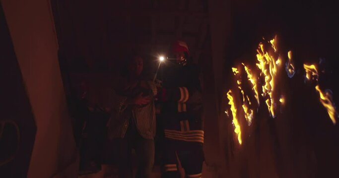 Brave Fireman Descends Stairs of a Burning Building and Holds Saved Girl in His Arms. Open fire and one Firefighter in the Background.