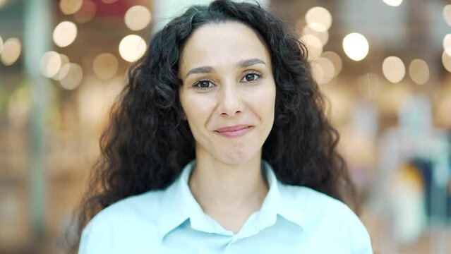 Close up portrait of a happy Hispanic woman laughing face young curly haired pretty brunette female looking at camera and smiling on a blurred background bokeh light Cheerful and joyful cute girl