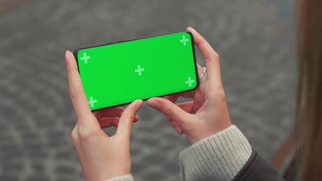 Young woman hands hold smart phone with horizontal green screen outdoors internet mobile smartphone technology city communication device use lifestyle slow motion