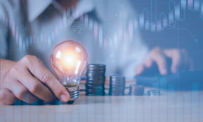 exposure man hand holding light bulb on wooden table and statistic graph, money saving and energy saving concept, financial planning or income and expense management, financial business background