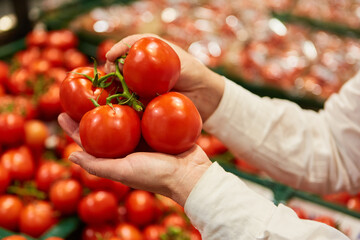 Hand eines Kunden hält frische Tomaten beim Einkaufen