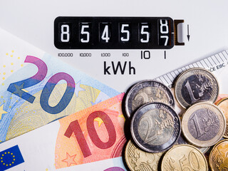 Close-up of electric meter and Euro notes and coins. Focus on kWh symbol. Concept for global energy...