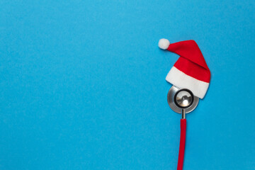 Medical red stethoscope with christmas hat on blue background. Christmas and New Year concept. Creative medical winter greeting card. Top view, flat lay, copy space