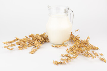 Oat milk in a jug and oat spike on light background. Vegan non dairy alternative milk.