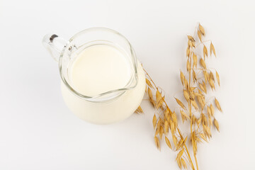 Oat milk in a jug and oat spike on light background. Vegan non dairy alternative milk.