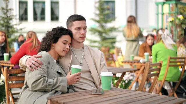 A happy couple outdoors near a cafe. Hugging each other, smiling, coffee. Autumn atmosphere