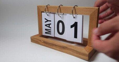 A man's hand setting the date in a desk calendar. Flip the calendar over to a perpetual calendar. Spring month. The May 1 - International Worker's Day. Holiday