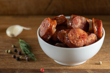 Slices of smoked pork sausages in a bowl on wood