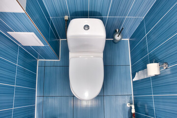 white toilet with closed lid in toilet with blue tiled wall. View of clean toilet bowl on top with...