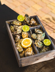 A variety of fresh oysters with lime and lemon in a wooden box. Fresh seafood. Outdoor cafe terrace. Blurred background with view of the yacht club.
