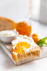 Sliced artisan homemade bread with ricotta or cottage cheese and orange jam on light background. Tasty breakfast. High key photography.